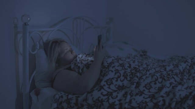 A fat woman lies in bed and checks her smart phoneat night.