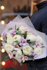 Young man florist holding big beautiful blossoming bouquet of purple tulips and white peonies flowers.