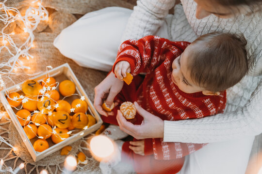 Christmas Celebration At Home In New Normal 2021. Family Celebrating Christmas In Time Of COVID Pandemic. Baby Toddler Girl With Mom Having Fun With Oranges, Tangerines With Numbers 2021.