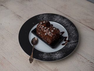 cake with chocolate cream on a plate decorated with a teaspoon next to it, a view from above, wooden bright background, warm atmosphere. place for text