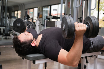 Fototapeta na wymiar Strong man wearing face mask lifting dumbbells at gym. Weight lifting concept. New normal.