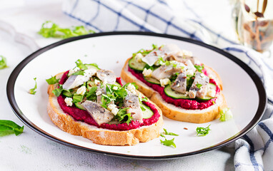 Herring fillet. Sandwich with salted herring and beetroot pate on the  toasts on white plate. Scandinavian cuisine.