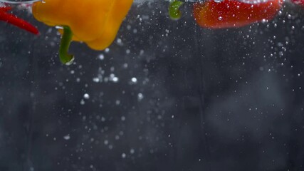 Super slow motion of coloured red chilli peppers, cherry tomatoes, bell pepper, fall into the water with bubbles. Filmed on high speed cinema camera - Powered by Adobe
