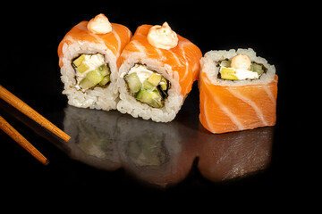 Sushi Sets Uramaki, California, Philadelphia, on a white plate. Festive, New Year concept. Against a dark reflective background.