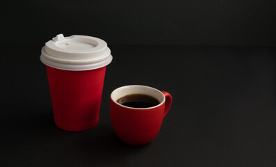 Red paper cup for coffee and a small red cup with coffee on a black background.