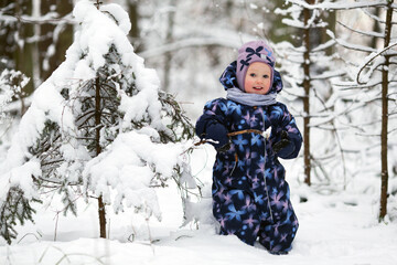 Cheerful smiling toddler girl wearing winter clothes having fun outside in snowy forest