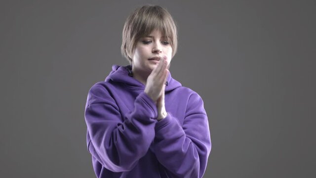 Cute young caucasian girl in hoodie rubs hands trying to keep warm on gray studio background