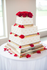 square white tiered wedding cake with red roses and gold accents