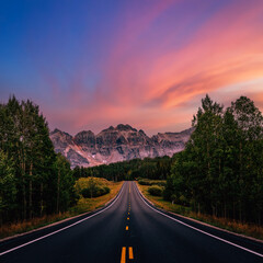 A long straight road leading towards mountains, Colorado, USA.  Road trip, traveling vibes, freedom, courage. Amazing sunset sky, dreamy landscape