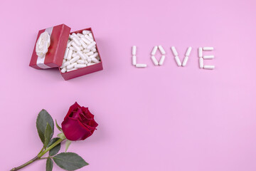medical capsules in a gift box, red rose and the word love on a pink background