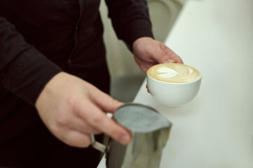 Fototapeta na wymiar Hands of baristas holding in one hand a cup of latte and in the other the rest of milk