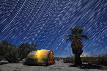 Illuminated Camping Tent Under a Full Moon and Star Trails