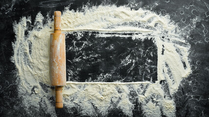Wooden rolling pin and flour. Bakery on a black stone background. Top view. Free space for text.