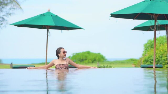 Adult Woman Standing Alone in Hotel Swimming Pool with Green Umbrellas
