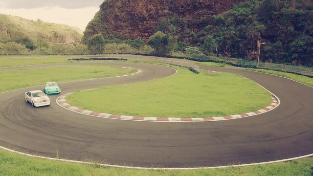 Two high performance cars drifting or sliding around hairpin turn of race track. Tilt up shot.