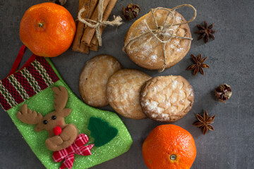 Christmas stocking, cinnamon sticks, tangerines and cookies on dark gray background with copy space. Festive decorations top view photo. 
