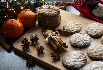 Fototapeta na wymiar Christmas biscuits with festive decoration. Top view photo of homemade cookies, Christmas lights, tangerines, star anise and cinnamon sticks.  