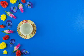 Obraz na płótnie Canvas Flowers composition with decorative saucer and cup on a plain blue background with place for text, top view