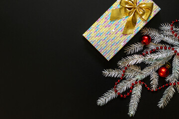 Silver spruce branch, christmas red beads, beautiful red Christmas balls, gift on a dark black background. Flat design. Copy space. View from above.