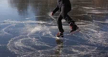 A young man is ice skating on a pond on a beautiful sunny day. Selective focus.