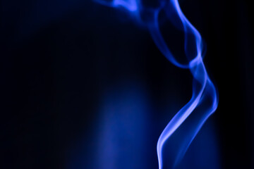 Obraz premium Blue color smoke from an Indian incense. Curvy lines in the darkness. Wind blows the smoke.