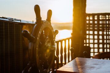 Wooden Helm or steering wheel of a shipping vessel with a sunrise in the background. Indicative of journey and transportation