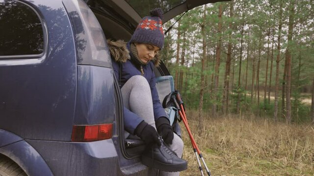 Woman sitting on car and fixing boots before hiking