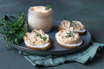 Sandwiches with smoked salmon and soft cream cheese pate or mousse with thyme and rosemary on a ceramic plate, green concrete background.