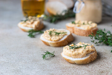 Homemade pate, spread or mousse in glass jar with sliced bread and herbs, light concrete background.