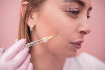 The girl injects herself in the face on a pink background.Cosmetology, salon, personal care.