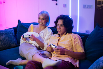 Handsome young man teaching how to play the video games to his girlfriend, on the couch, concept about home entertainment, video games.