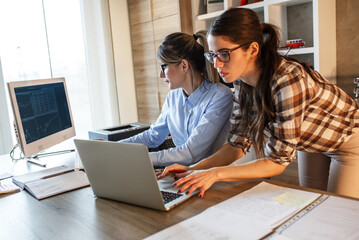 Two female office workers using computer and discuss about business project.Teamwork.	
