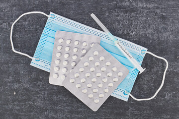 Pills, medical face mask, syringe on a gray background, top view. First aid, care during illness.