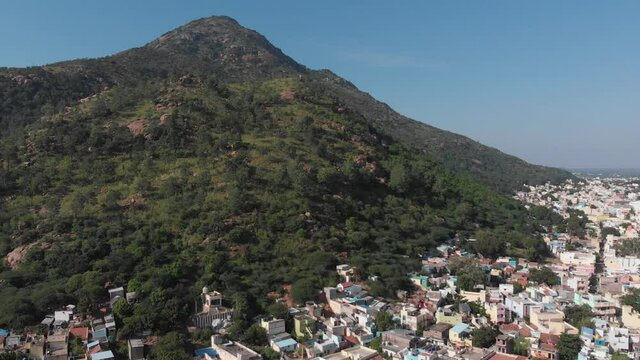 Aerial shot of residential houses in front of giant overgrown mountain during beautiful weather in Tiruvannamalai,India.