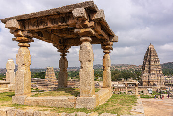 Hampi, Karnataka, India - November 4, 2013: Virupaksha Temple complex. Ruinous brown stone baldachin on hill above said temple, showing Shiva Vimanam and Gopuram at right. Landscape with gray cloudsca © Klodien