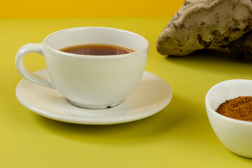 Healing tea, coffee and pieces of birch chaga in a white cup on a yellow background. Naturopathy. Alternative medicine. A trendy superfood for immunity. Natural antioxidant.