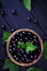 Black currant and green leaves on a dark wooden background. Background with currant berries and green leaves. Currant Macro