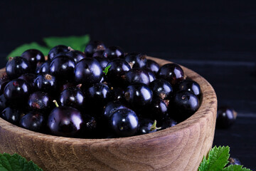 Black currant and green leaves on a dark wooden background. Background with currant berries and green leaves. Currant Macro