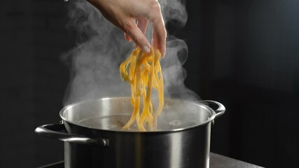 Female chef putting raw pasta into boiling water. White smoke in slow motion rising above hot saucepan on black background. Cooking in restaurant. Delicious Italian pasta. Full hd - Powered by Adobe