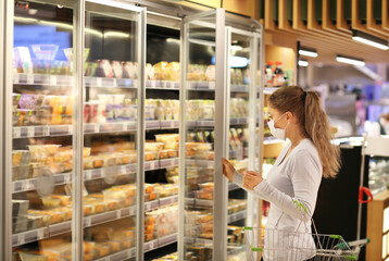 Woman choosing frozen food from a supermarket freeze.Supermarket shopping, face mask