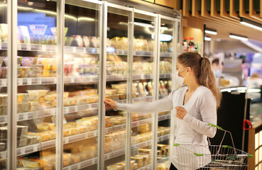Woman choosing frozen food from a supermarket freeze.Supermarket shopping, face mask