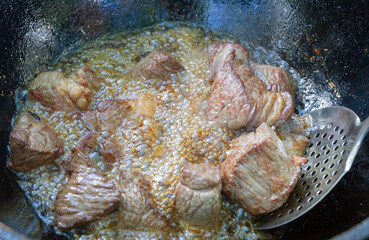 Cooking pilaf in a cauldron on the grill outside in the summer