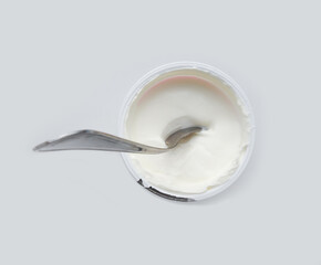 An open jar of sour cream or yogurt with a foil lid and a spoon on a white background. Horizontal orientation. View from above.