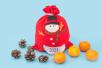 red sack of Santa Claus with tangerines and pine cones on a blue background. New year 2021.
