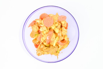 Top view of turmeric chicken with carrots, tomatoes and corns in a purple bowl over wooden background. 