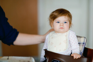 Father feeding baby girl from spoon mashed vegetables and puree. food, child, feeding and people concept -cute toddler, daughter and dad with spoon sitting in highchair and eating at home.