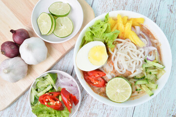 Noddle in Tangy Fish Gravy or Laksa Utara is a Special Malaysian Food Popular in Penang in a white bowl served with egg, lime, cucumber, chilies, pineapples and salad. Selective focus.