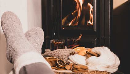 mulled wine by the fireplace, 2 glasses of drink, spices, a warm scarf and feet in warm socks near...