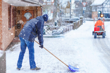 Man with snow shovel cleans sidewalks in winter during snowfall. Winter time in Europe. Young man...