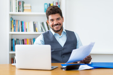 Laughing hispanic businessman with computer and paperwork